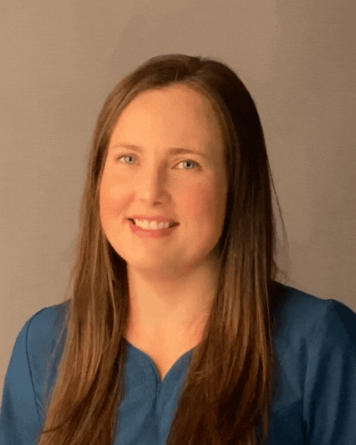 A woman with long brown hair is wearing a blue shirt and smiling for the camera.