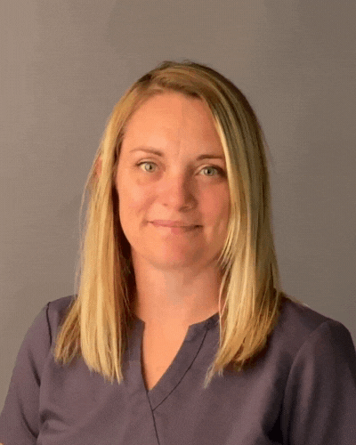 A woman in a purple scrub top is smiling for the camera.