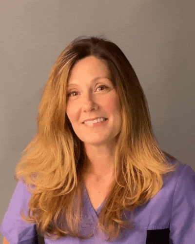 A woman in a purple scrub top is smiling for the camera.