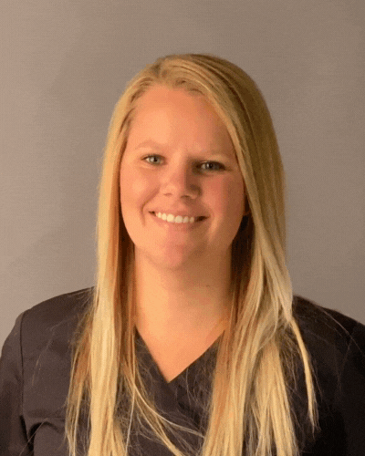 A woman with long blonde hair is smiling and wearing a black scrub top.
