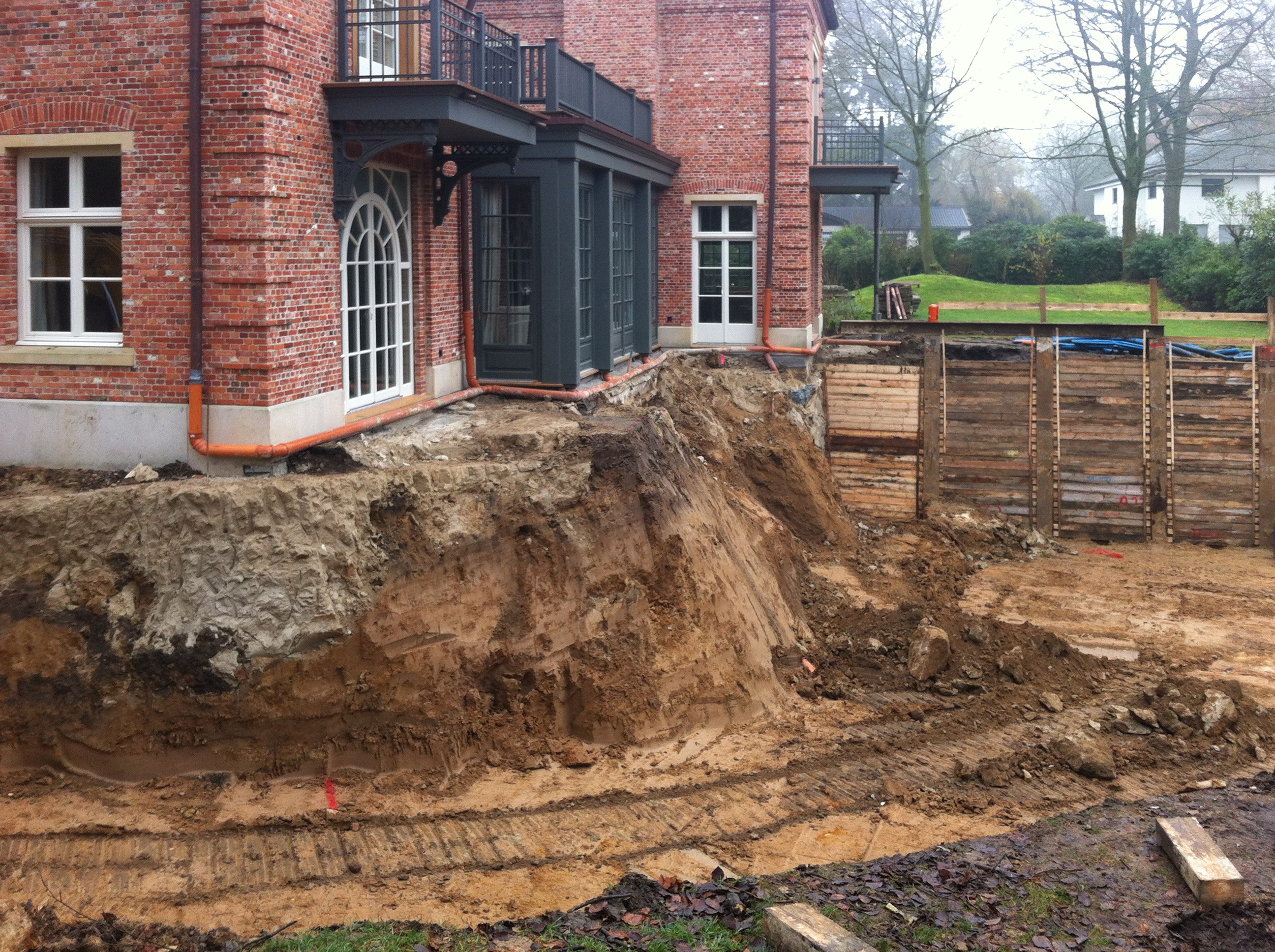 Vor einem im Bau befindlichen Backsteinhaus liegt ein großer Erdhaufen.