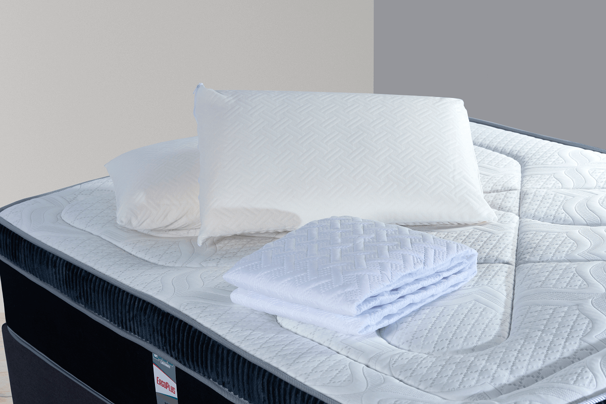 Almohadas y toallas blancas dobladas sobre un colchón con borde azul, en el interior.