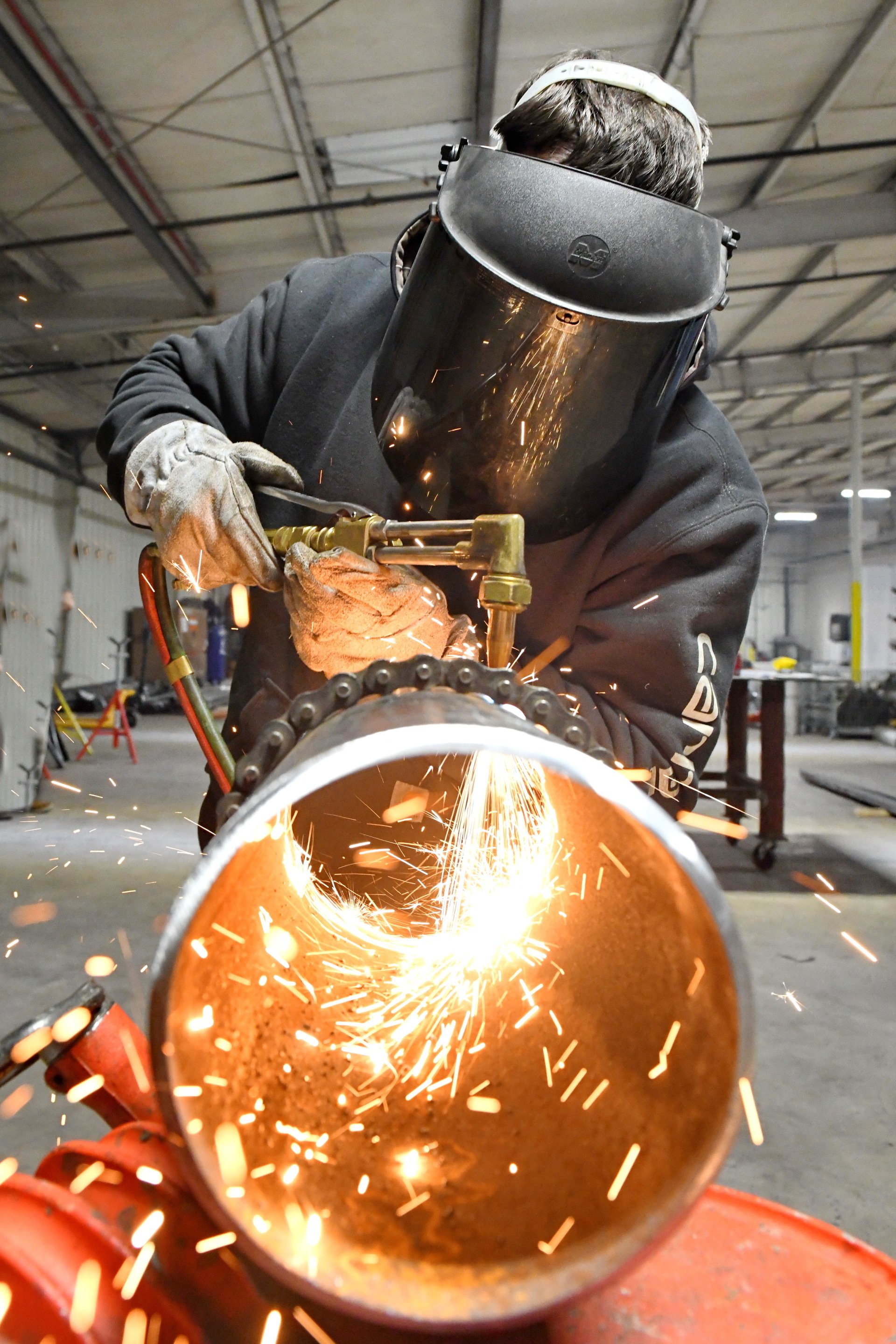 Apprentice using a plasma cutter to split a pipe for pipefitting while wearing a welding mask