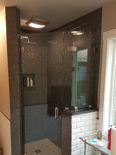Dark tiled shower with glass doors, built-in shelf, and a white subway tile accent on the exterior wall.
