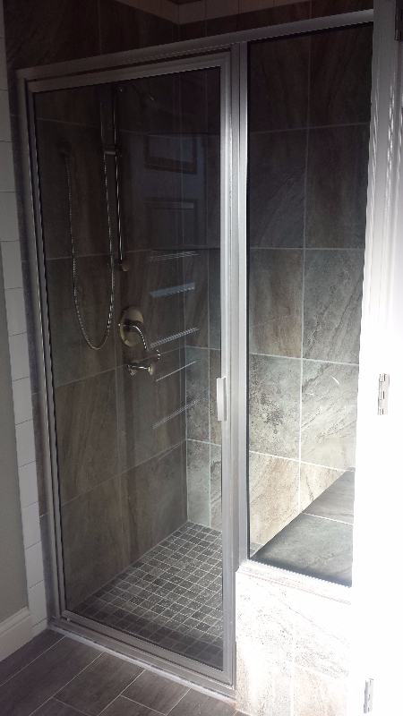 Glass shower enclosure with gray tile walls and floor. Silver fixtures.
