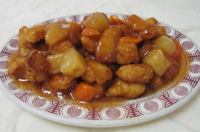 Sweet and sour chicken with pineapple and carrots on a patterned plate.