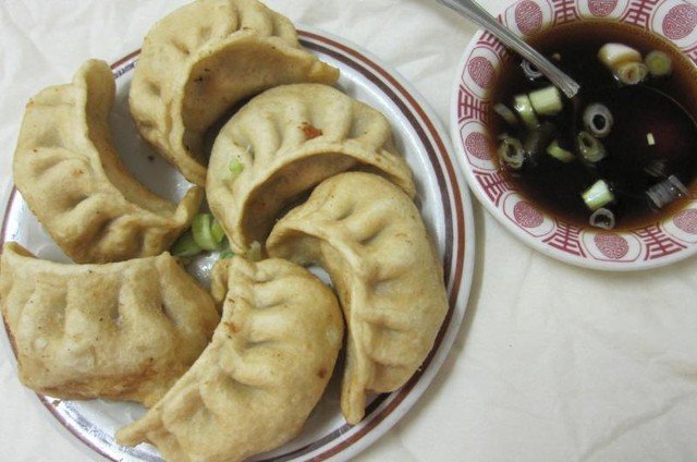 Plate of fried dumplings with dipping sauce and scallions.