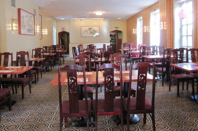 Interior of a Chinese restaurant; tables with red chairs, cream walls, and floral patterned carpet.