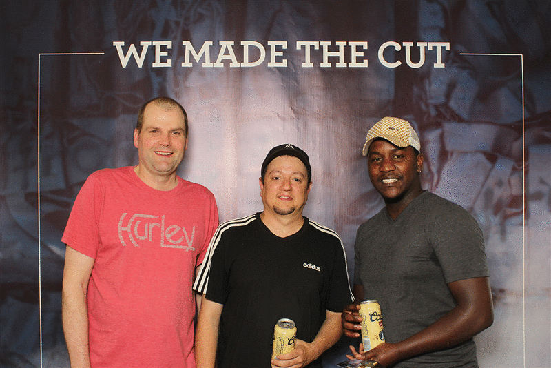 Three men are posing for a picture in front of a sign that says we made the cut