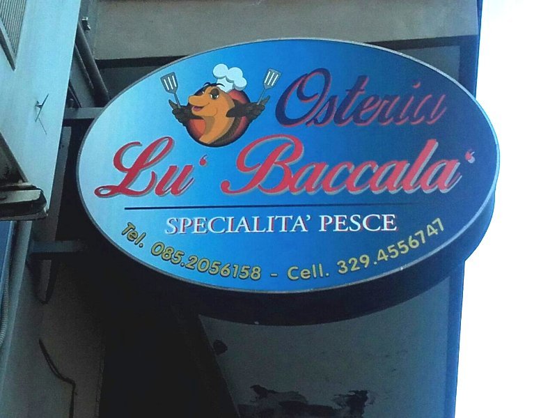 baccalà tagliato a fette con accanto, cipolla,aglio e foglie di alloro, il tutto appoggiato su un sacchetto di carta marrone