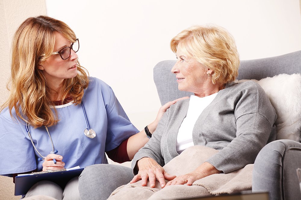 A nurse is talking to an elderly woman who is sitting in a chair.