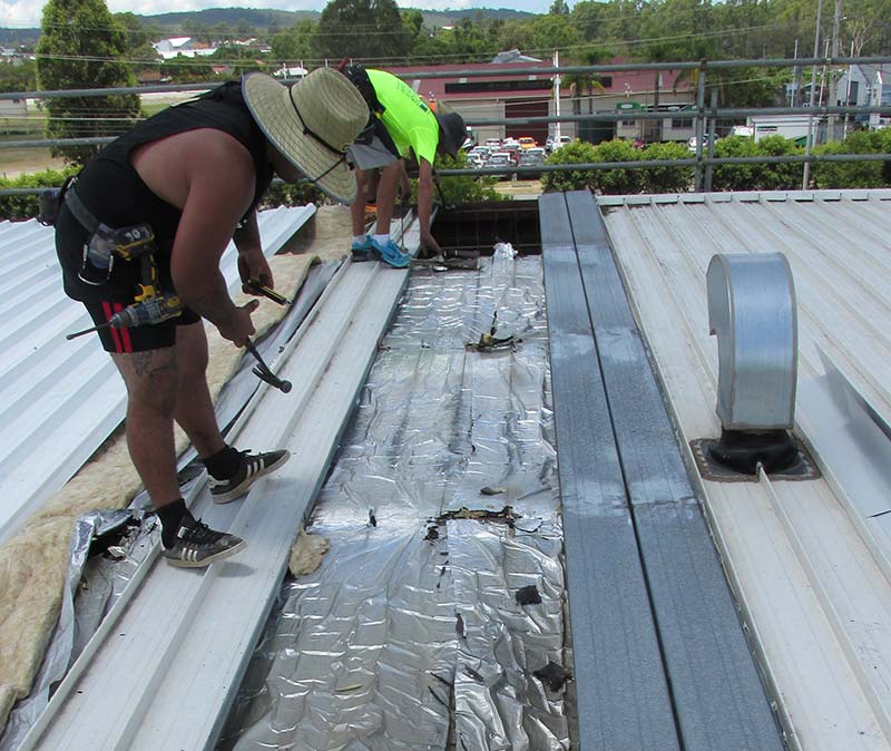 two men standing on a roof taking the sheeting off of the roof
