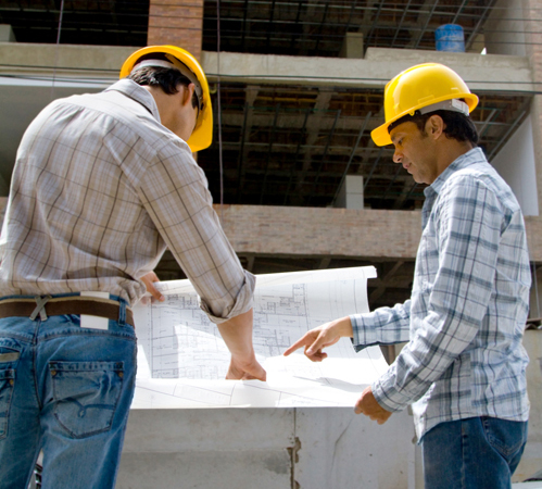 Experienced builders at construction site discussing a building's map to provide reliable services in New Plymouth, NZ