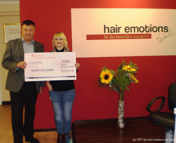 Ein Mann und eine Frau halten einen Scheck vor einem Schild mit der Aufschrift „Haaremotionen“