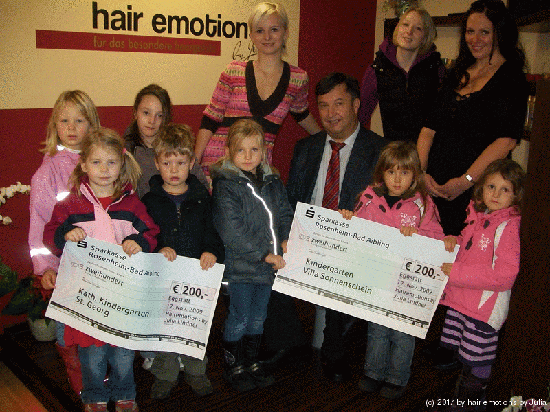 Eine Gruppe von Kindern hält Schecks vor einem Haar-Emotionsschild