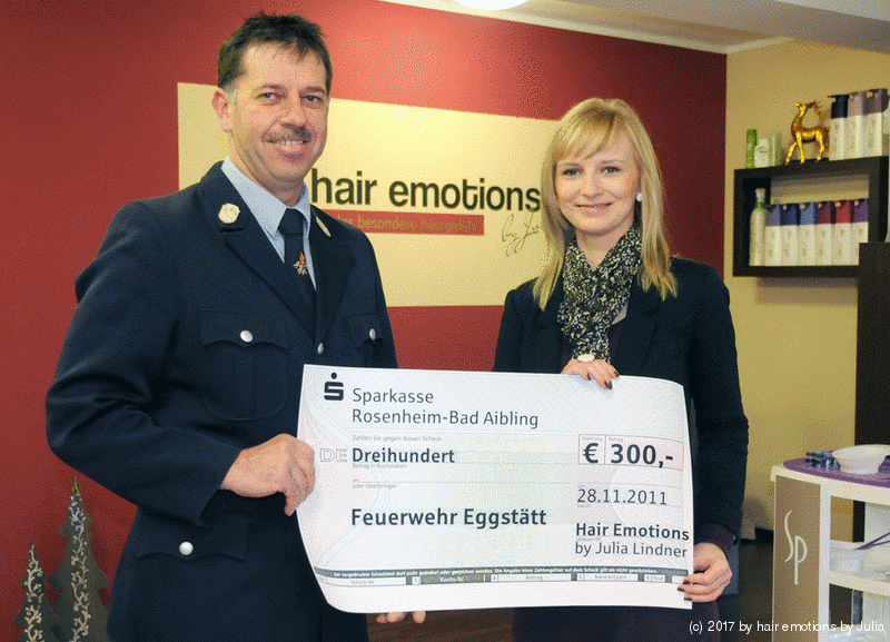 Ein Mann und eine Frau halten einen Scheck vor einem Schild mit der Aufschrift „Haaremotionen“