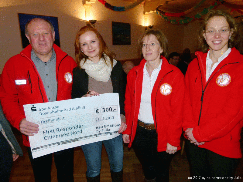 Eine Gruppe von Menschen in roten Jacken hält einen Scheck über 300 Euro