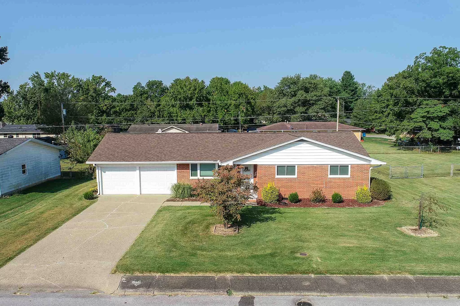 An aerial view of a brick house with a white garage and a lush green yard.