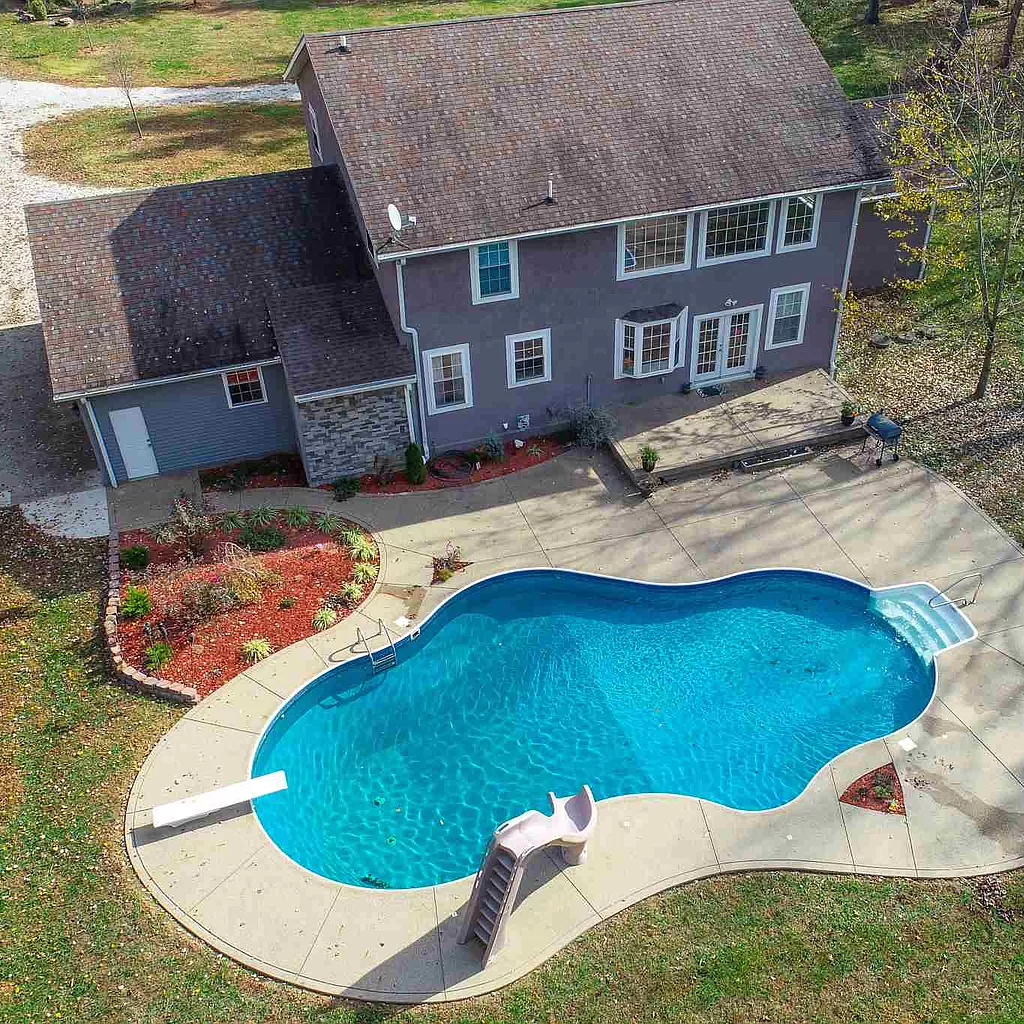 An aerial view of a house with a large swimming pool in front of it.