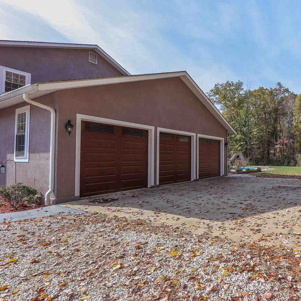 A house with three garage doors and a driveway filled with leaves.