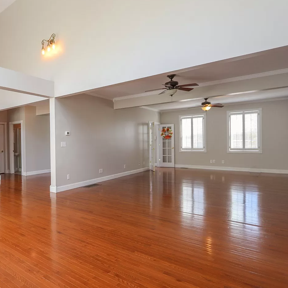 A large empty room with hardwood floors and a ceiling fan.