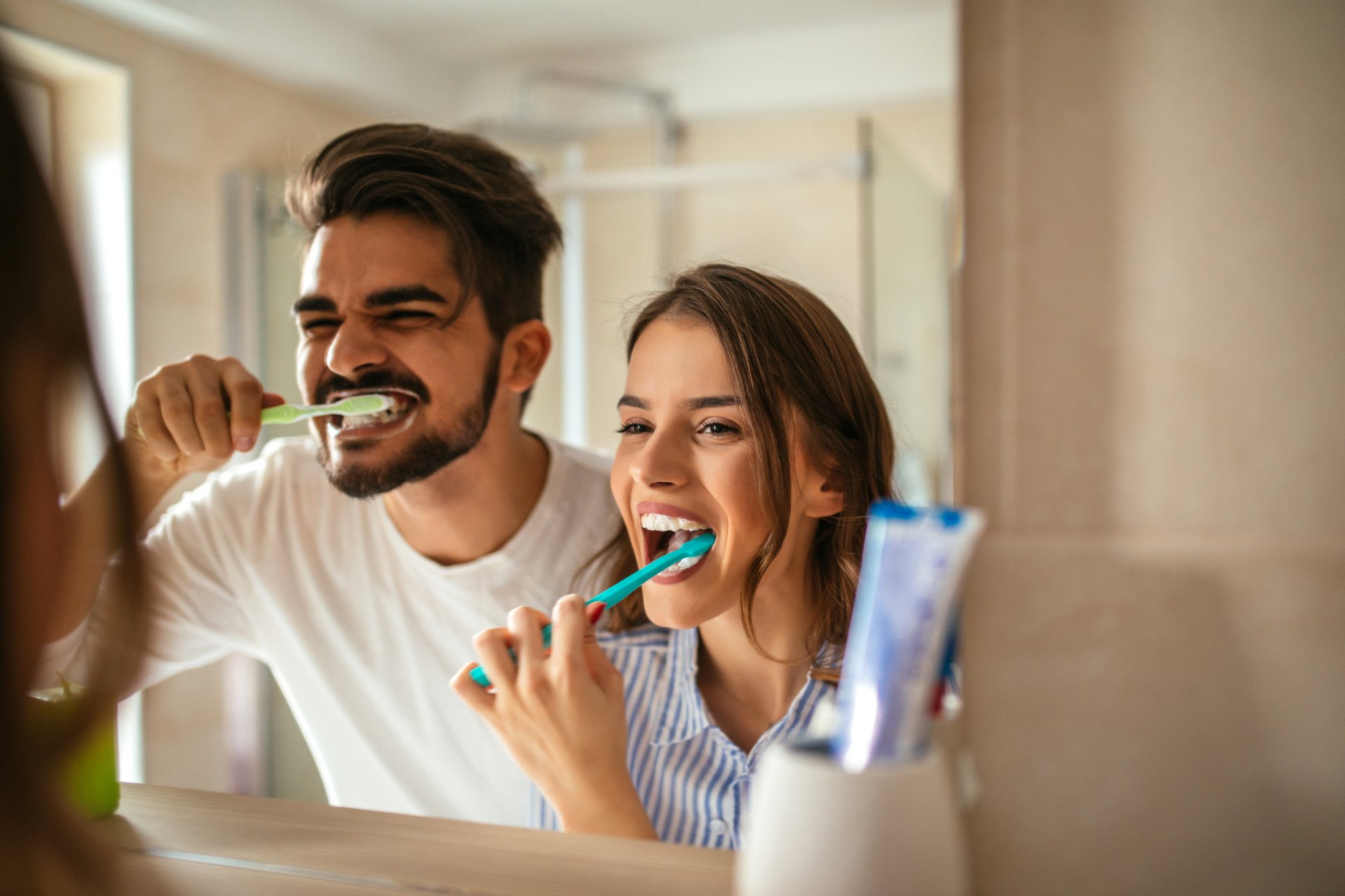 Man and a woman brushing teeth in a mirror
