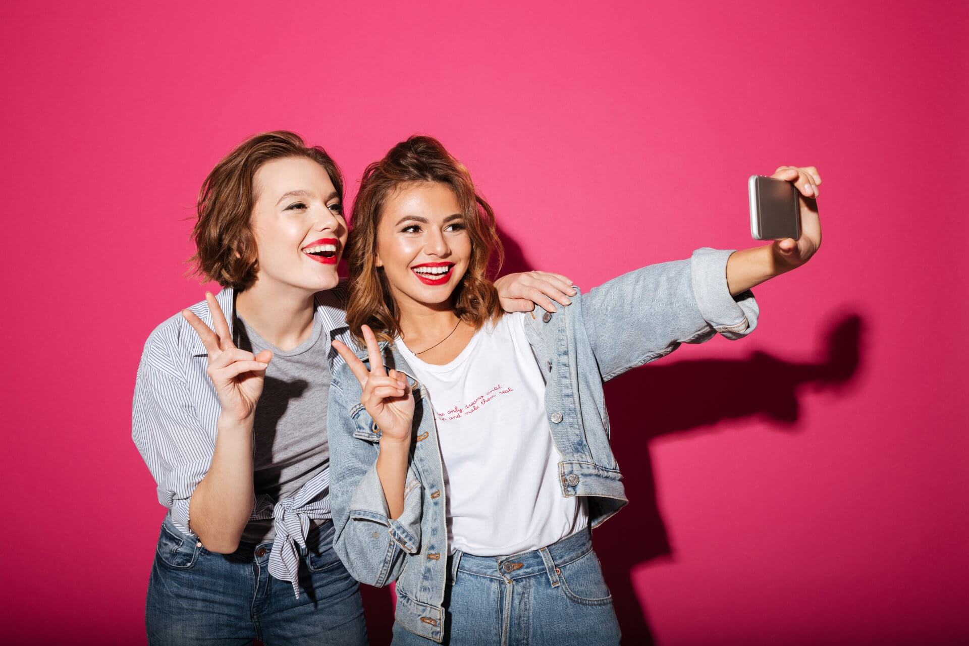 2 Girls taking a selfie showing their white teeth with a pink background