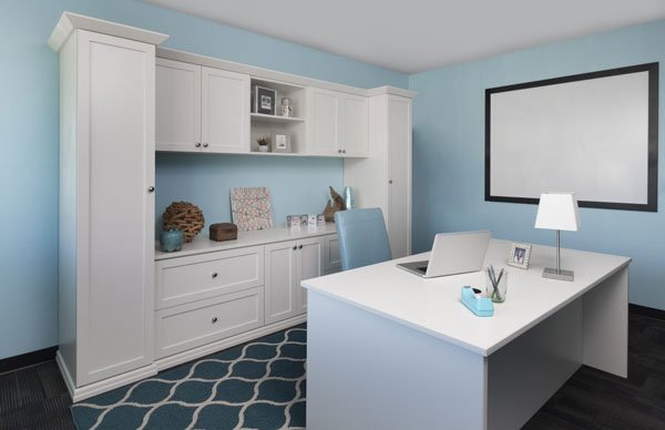 A home office with blue walls and white cabinets