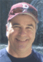 Man smiling, wearing a maroon baseball cap with a white 