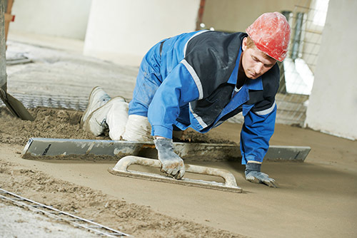Plasterer at indoor concrete cement floor topping with float