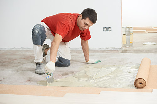 Worker carpenter doing parquet Wood Floor work gluing down cork 