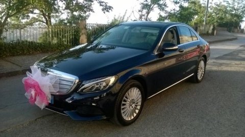 Un'auto nera con un fiocco rosa sul davanti è parcheggiata sul ciglio della strada.