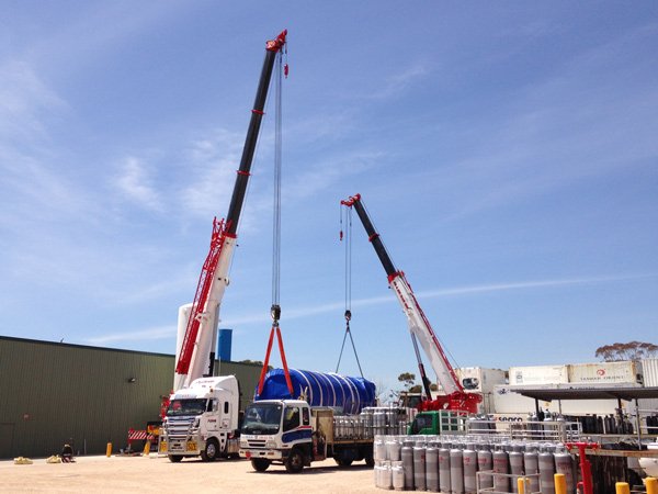 two cranes lifting blue tube