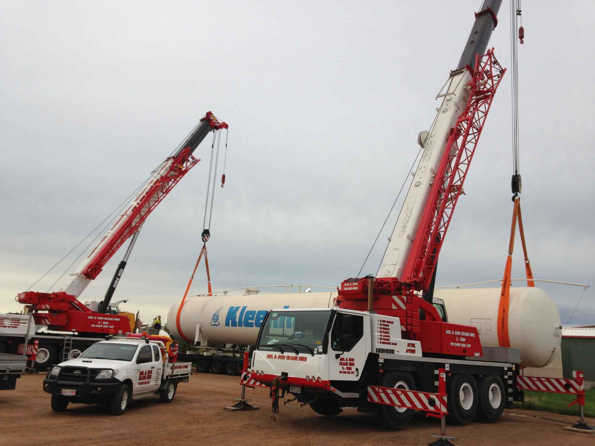 two red cranes lifting giant pipe