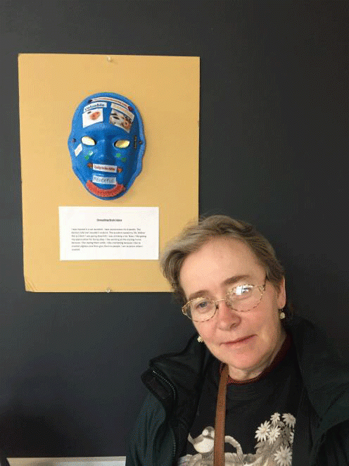 A woman stands in front of a blue mask on a wall