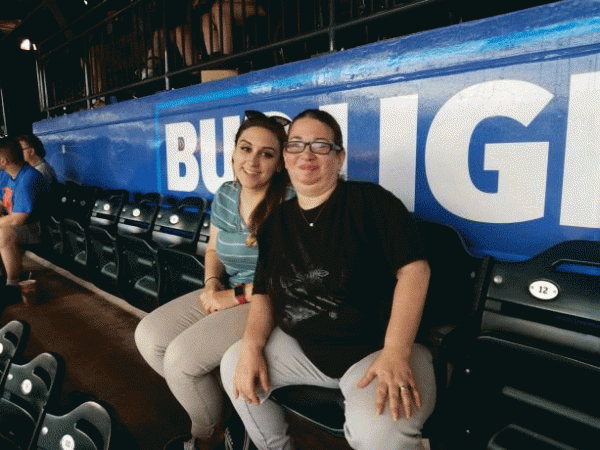 Two women are sitting in a stadium in front of a sign that says bud light