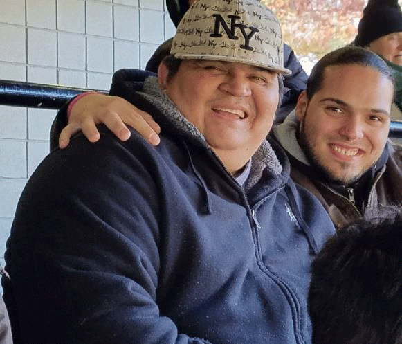 A man wearing a ny hat smiles with his arm around another man