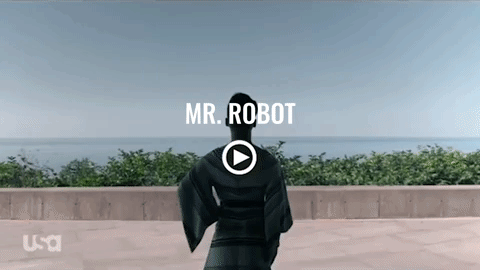 A man in a black suit is standing in front of a body of water.