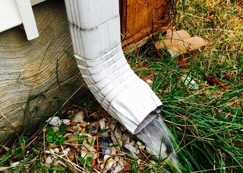 white gutter with rain coming out on grass