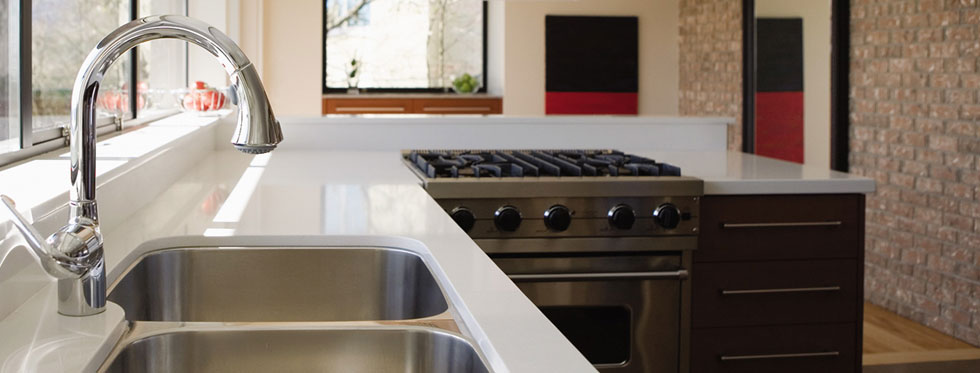 A steel sink and cooker hob set into a white marble kitchen worktop