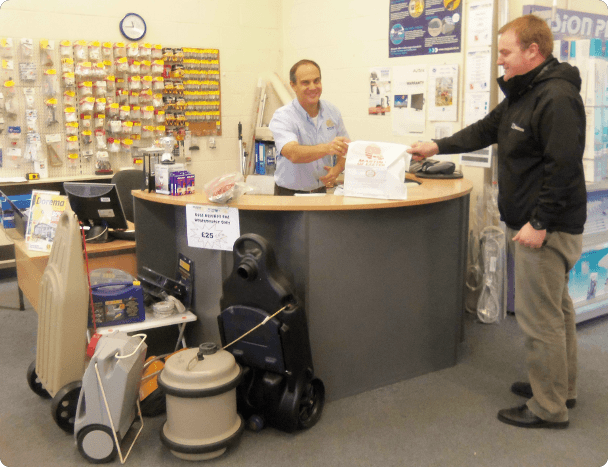 Man at till passing purchases to a customer in store