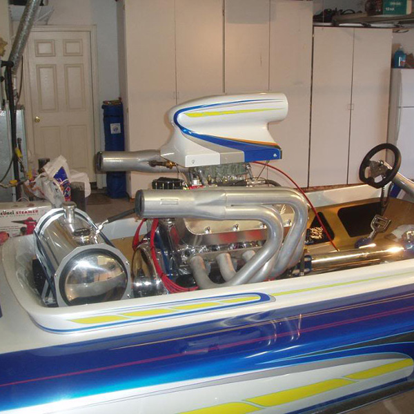 Blue-and-white drag boat with chrome engine in a garage