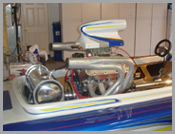 Custom racing boat with exposed engine and blue-striped hull in a garage