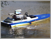 Blue and white racing boat floating on calm water, with an outboard motor and gear on board