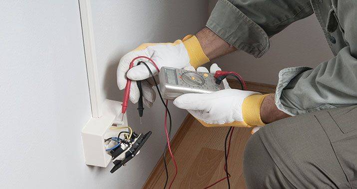 An electrician undertaking electrical testing work on a wall socket