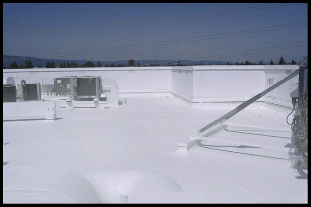 White commercial rooftop on a sunny day. Buildings and equipment are visible against the backdrop of mountains and a clear sky.