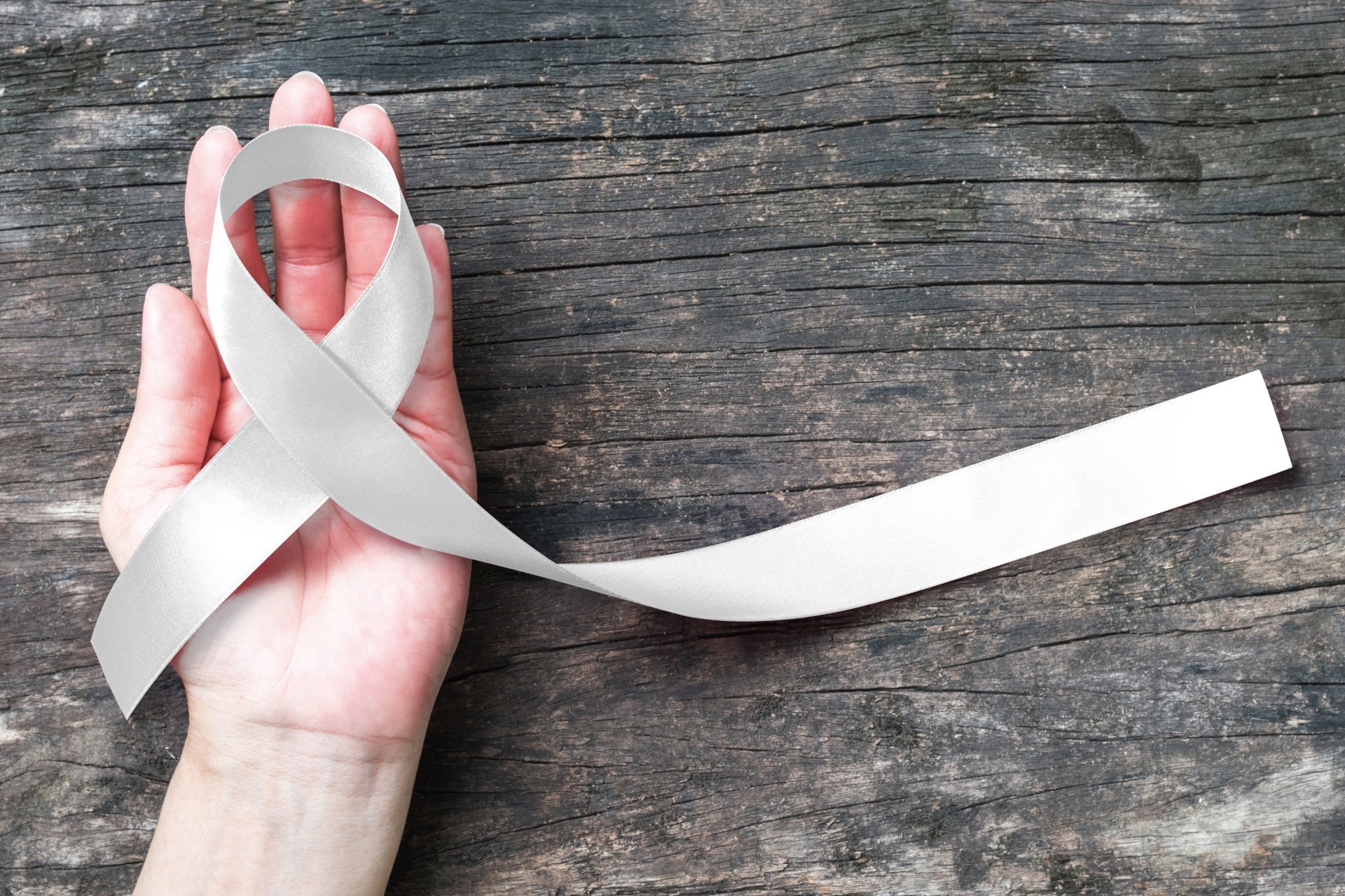 A hand is holding a white ribbon on a wooden table.