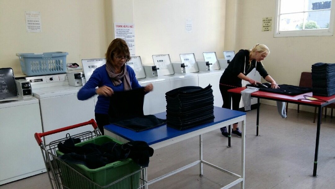man at laundromat sitting in front of a washing machine with a tablet