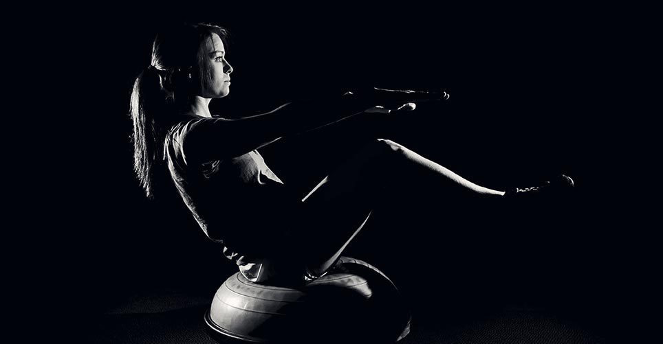 A woman is sitting on a pilates ball in the dark.